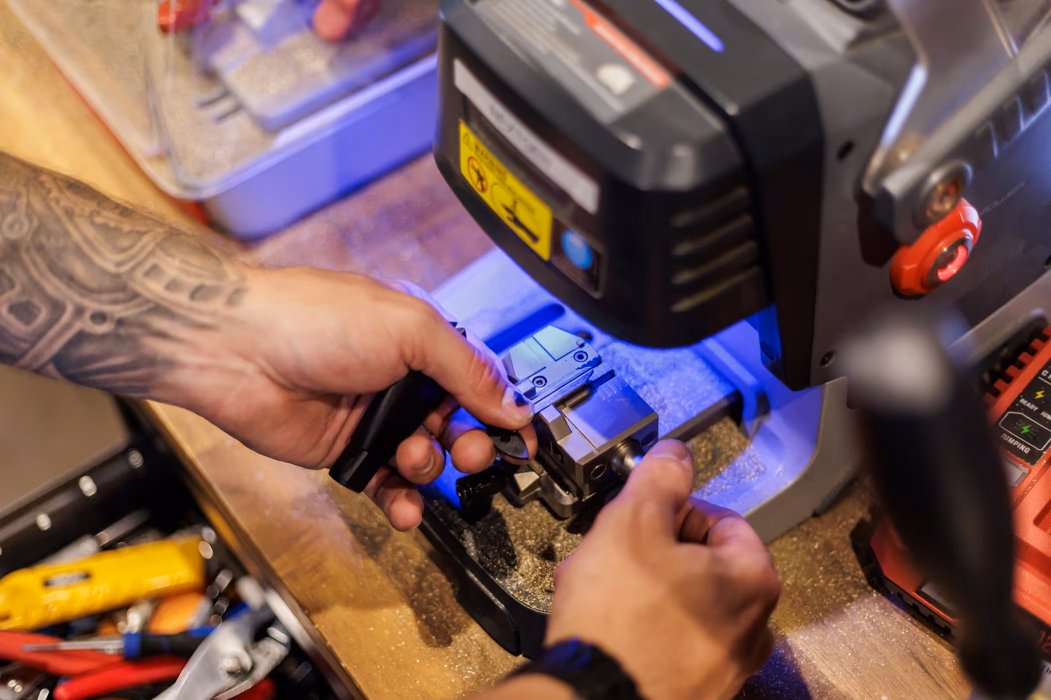 Person with tattooed arm operating a key cutting machine on a wooden workbench.