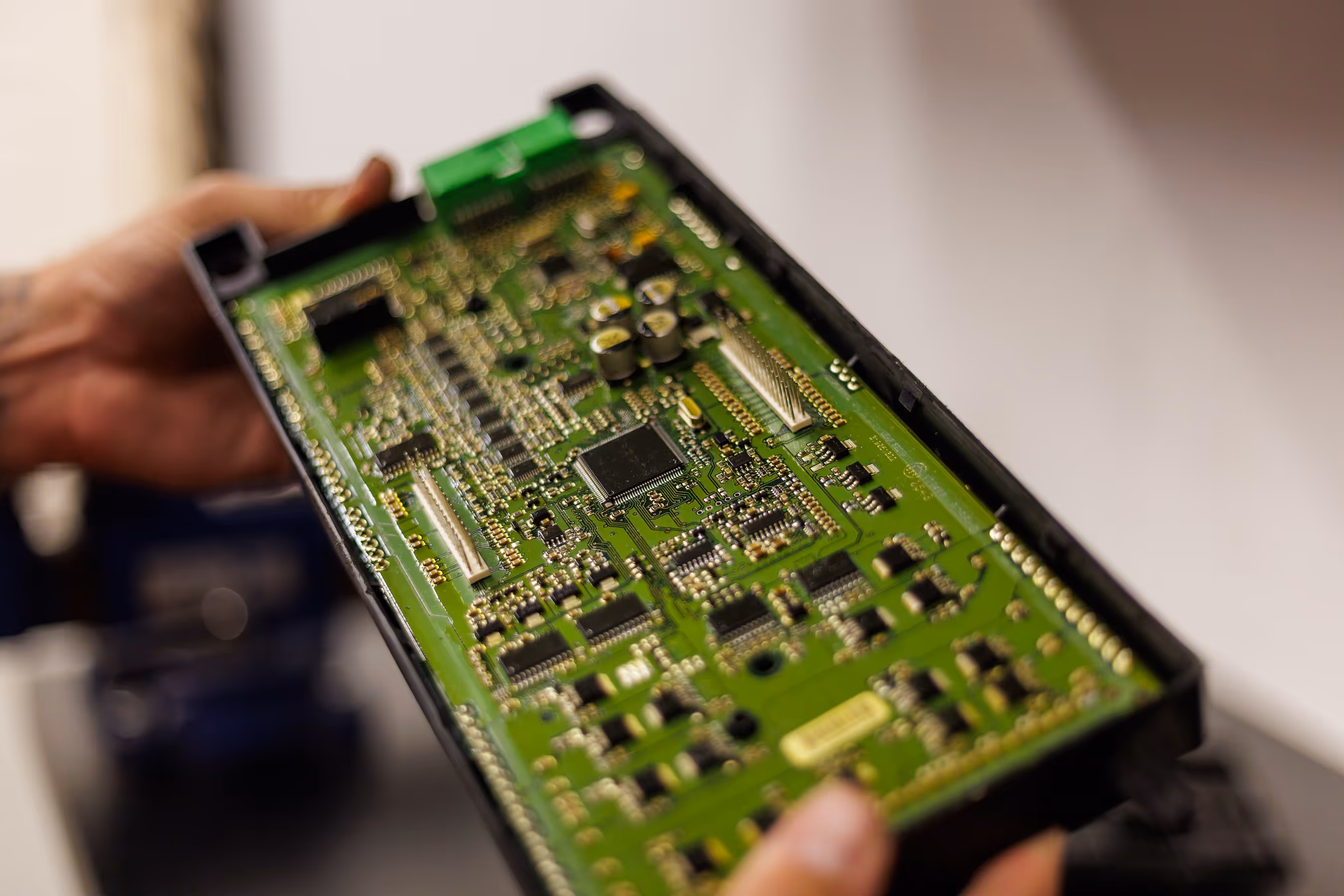 Close-up of hands holding a green printed circuit board with various electronic components.