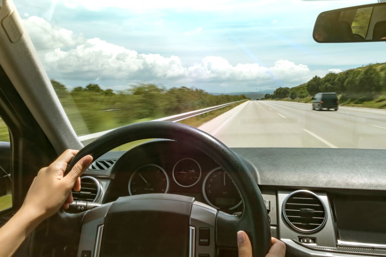 Person driving a car on a highway with clear skies and green surroundings.