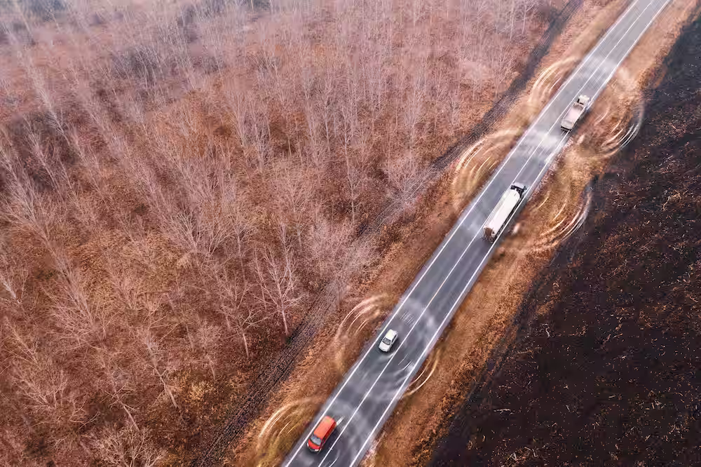 Aerial view of a two-lane road running through a bare forest with four vehicles and digital connectivity signals around them.