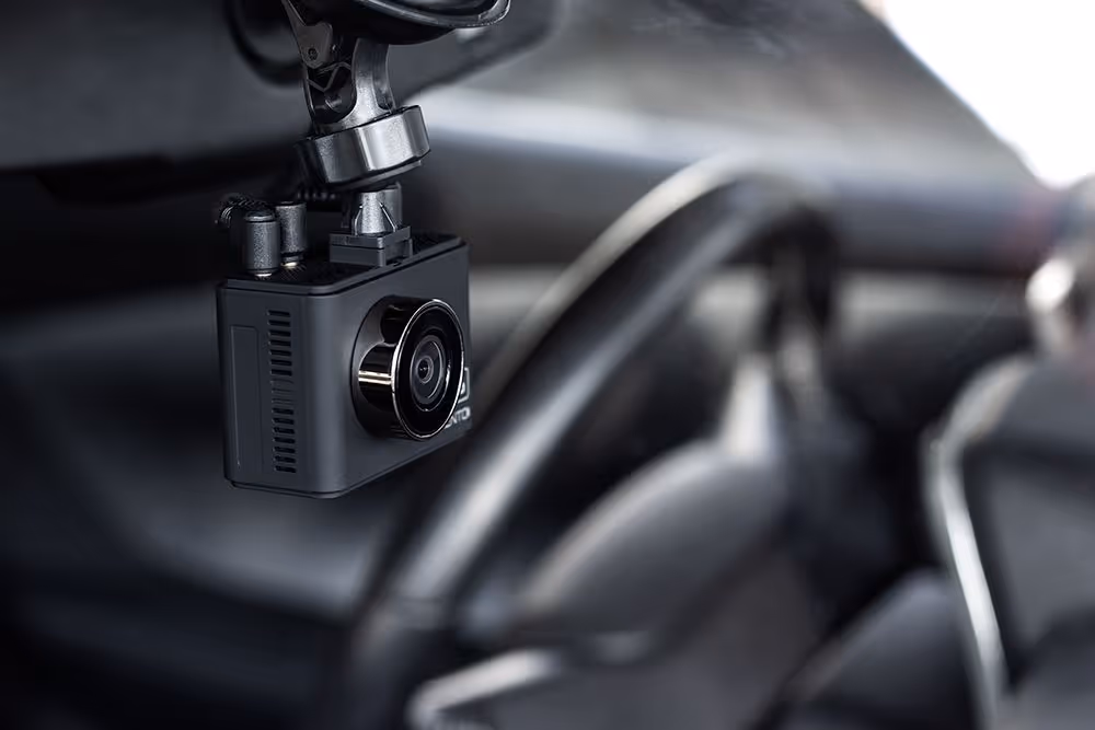 Close-up of a black dashboard camera mounted inside a car near the rearview mirror.