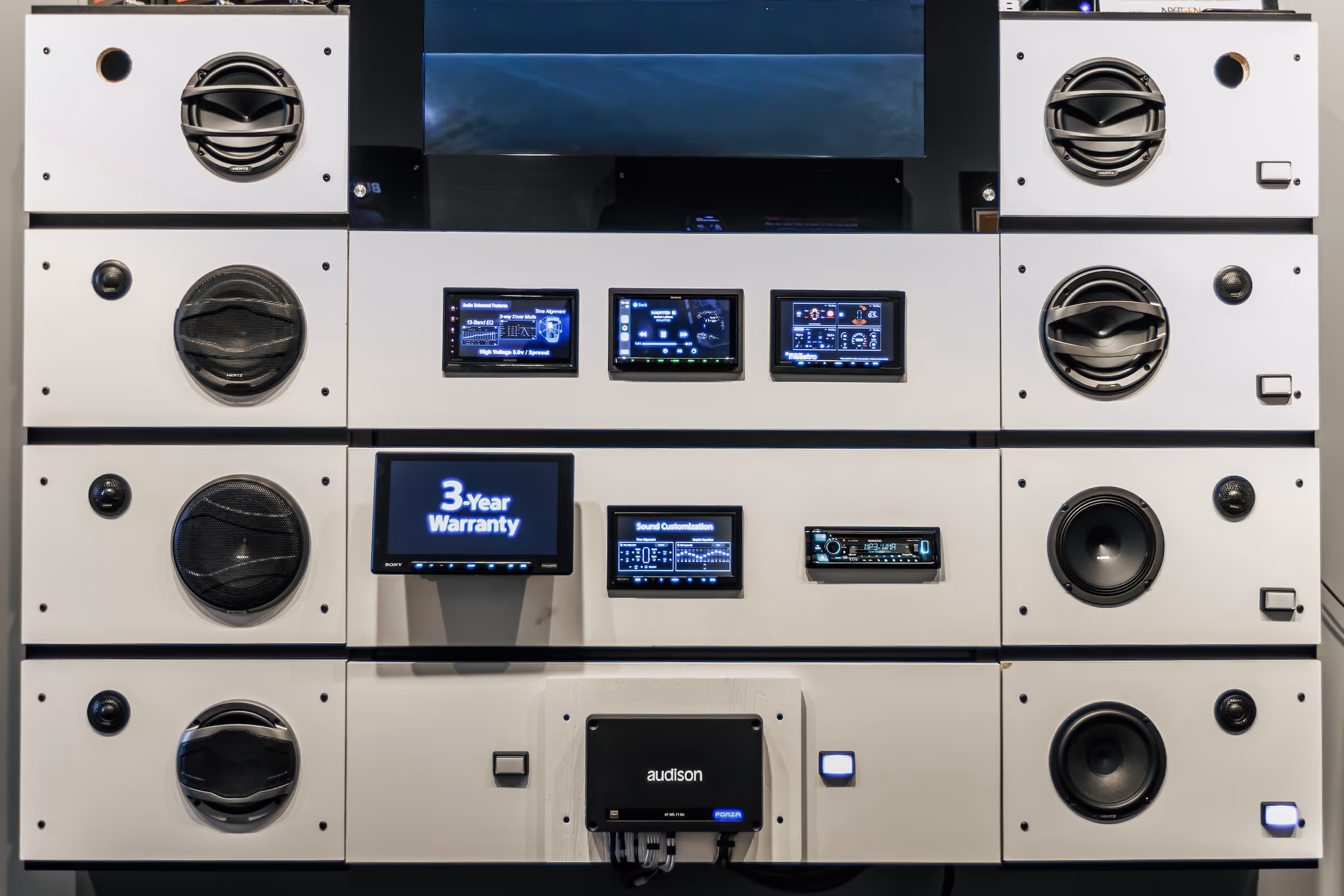 Wall-mounted audio system display with multiple speakers and digital control screens, including one showing '3-Year Warranty'.