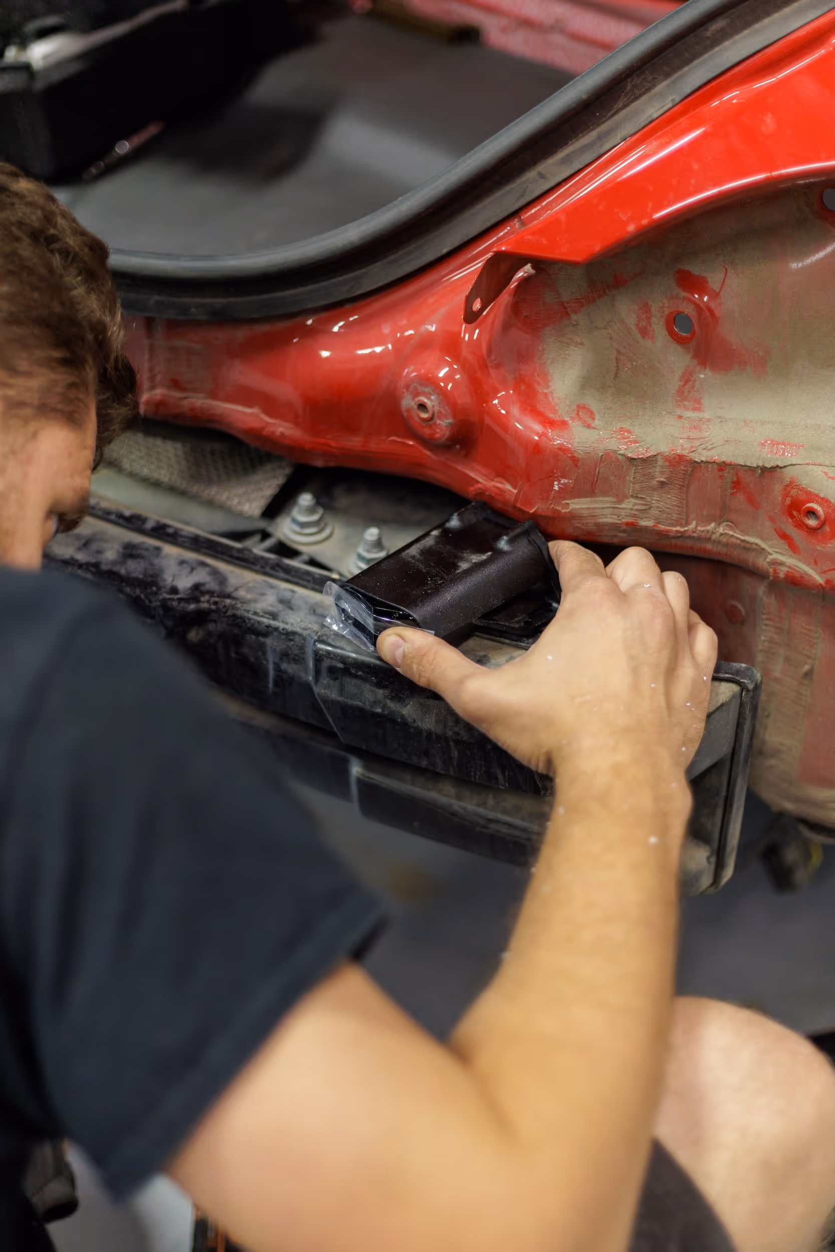 Man repairing or inspecting the inner part of a red car near the rear bumper.