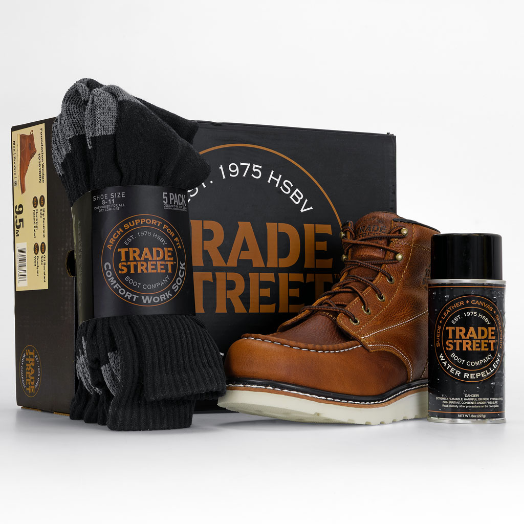 Trade Street Boot Company product kit featuring rugged brown leather work boots displayed alongside branded packaging, a black gear bag, and leather care accessories, arranged as a premium lifestyle flat lay that highlights craftsmanship, durability, and heritage workwear branding.