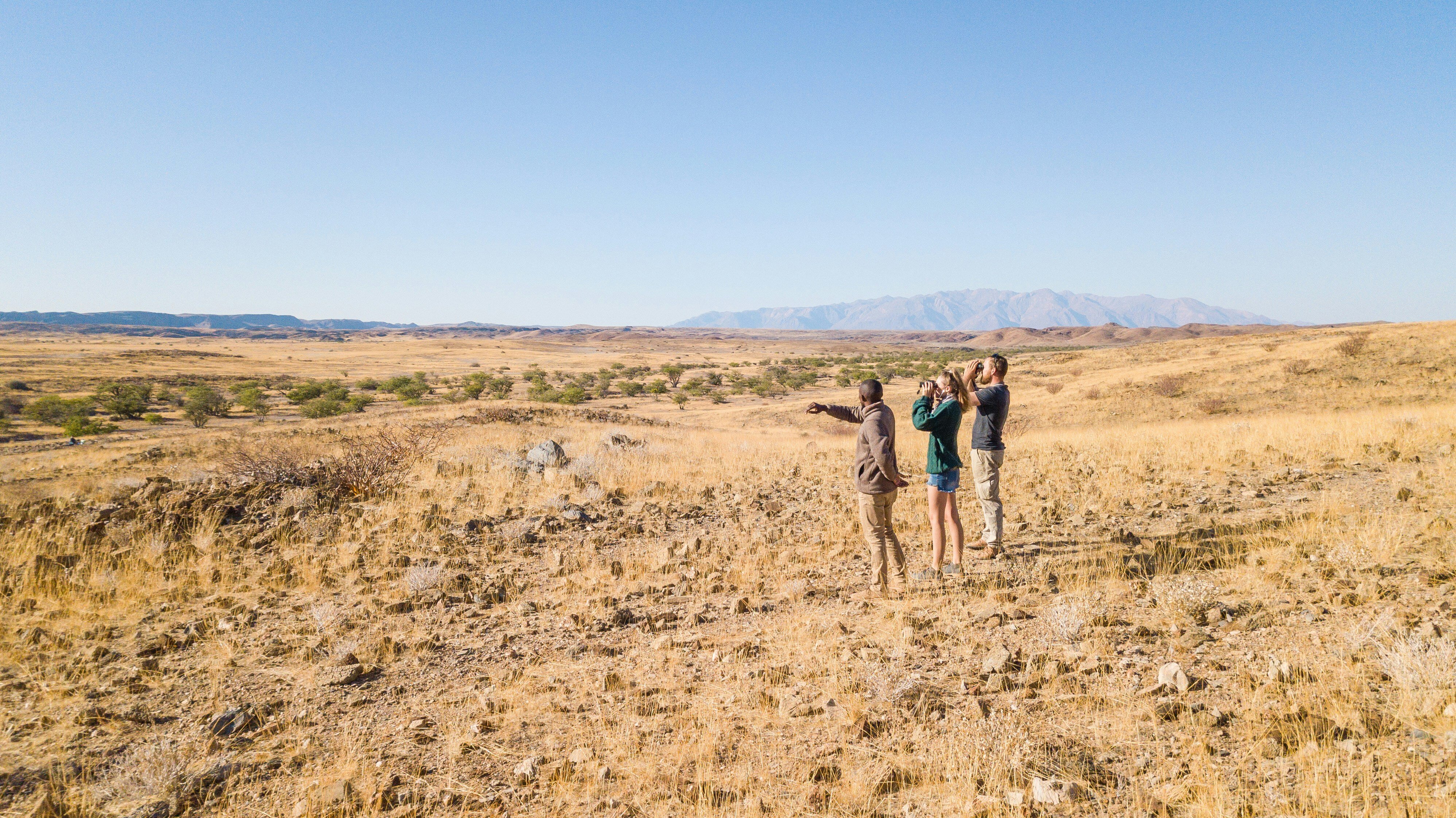 Zwei Personen, die sich zusammen mit einem Ranger auf einer Walking Safari befinden und die durch ihre Ferngläser schauen.