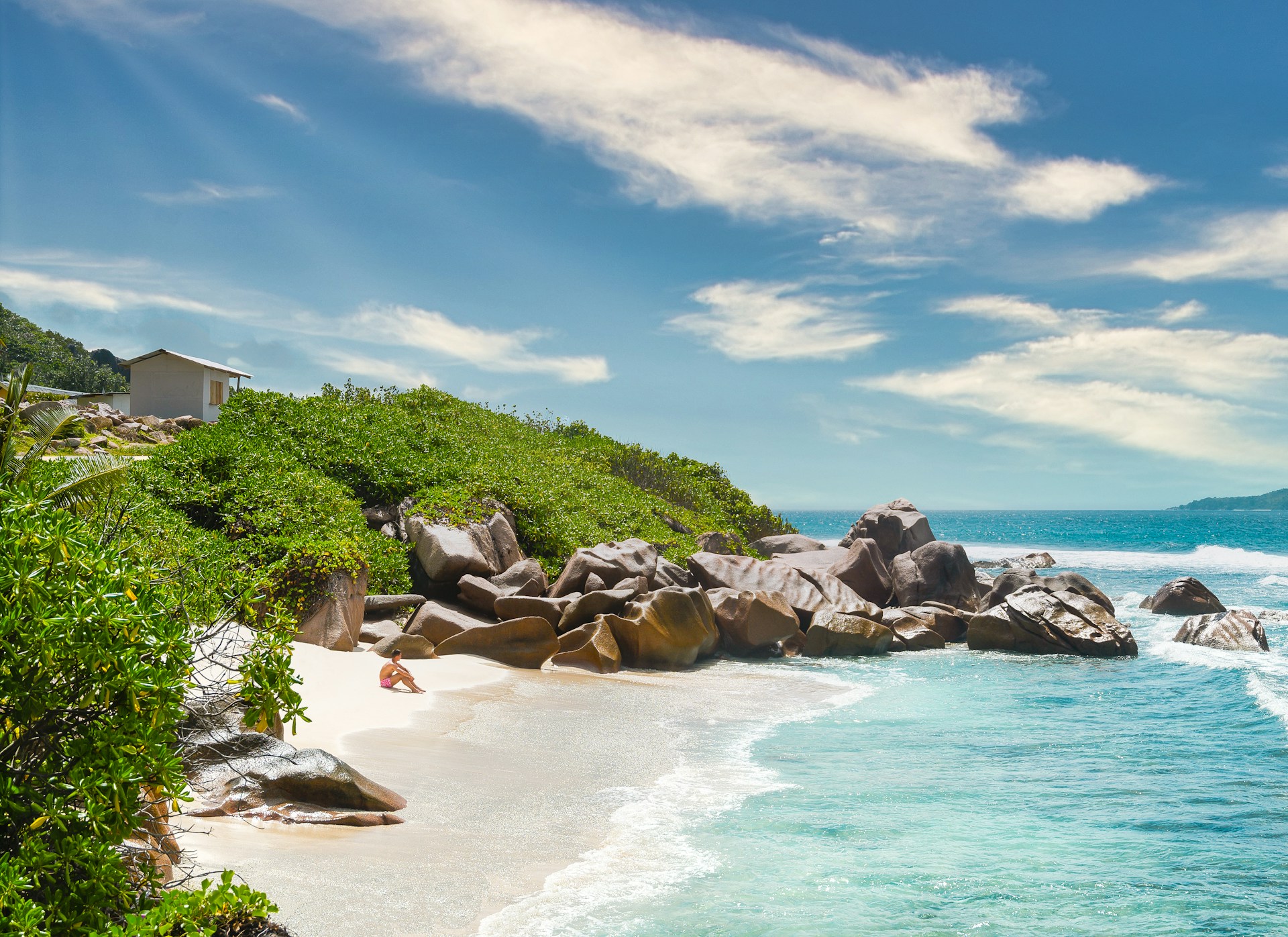 Kleine Sandbucht auf Praslin mit den typischen Granitfelsen der Seychellen, eine Person sitzt am Wasser
