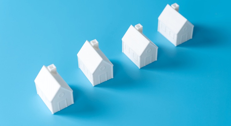 Miniature white houses on a blue background representing the housing market