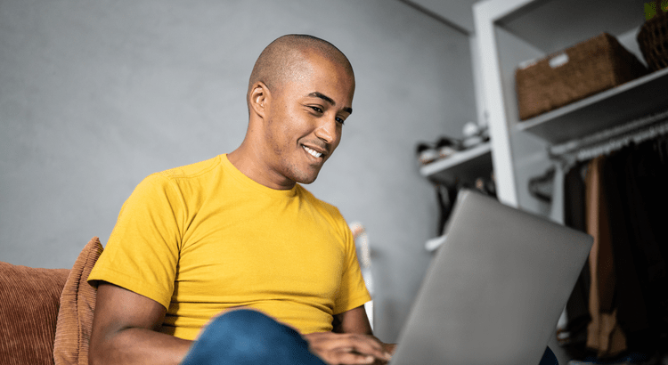 Man sitting on a sofa and researching homes on a laptop.
