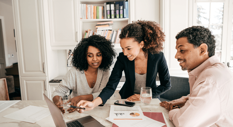Two home buyers review documents with a real estate professional at a table.