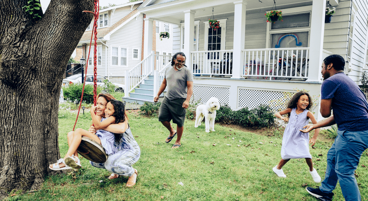 Two adults and two children play in the yard outside a two-story home.