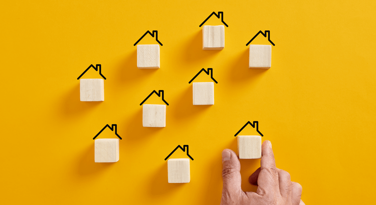 A hand arranging nine wooden house blocks on a yellow background