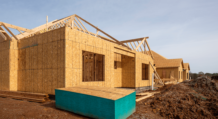 Wood-framed homes under construction with exposed roof trusses and stacked building materials.