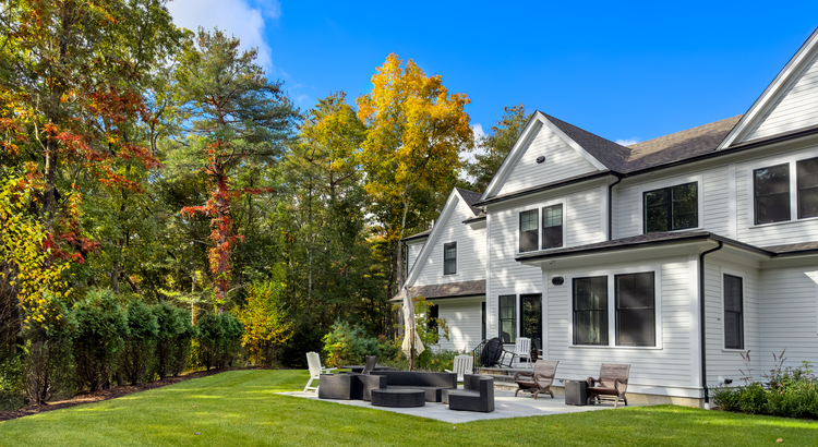 Gray 2-story house with a backyard patio, lawn, and trees with fall foliage.