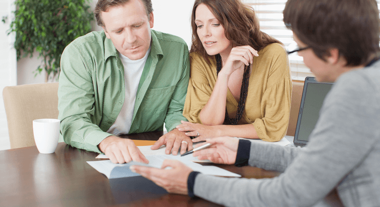 Two people reviewing paperwork with a third person at a table beside a laptop.