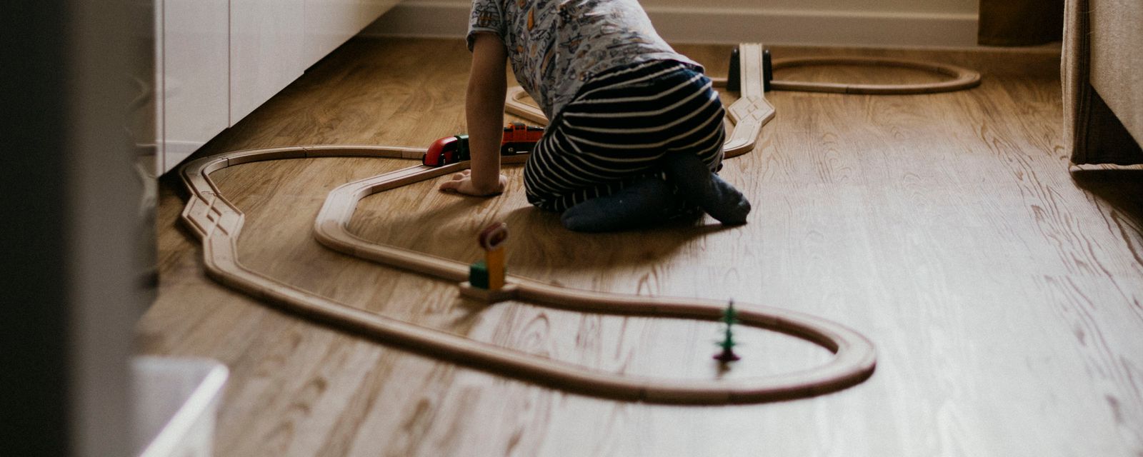 Toddler playing with a wooden toy train set on a matte wood floor