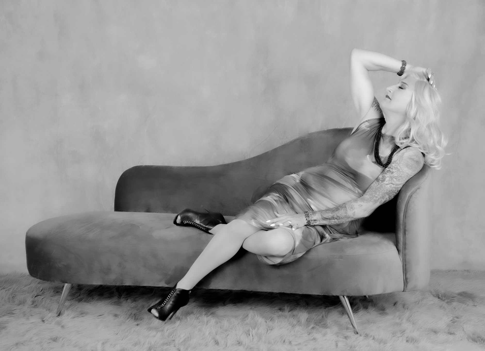 Confident woman posing on chaise lounge, showcasing bold tattoos and feminine attire, Boudoir Photography.