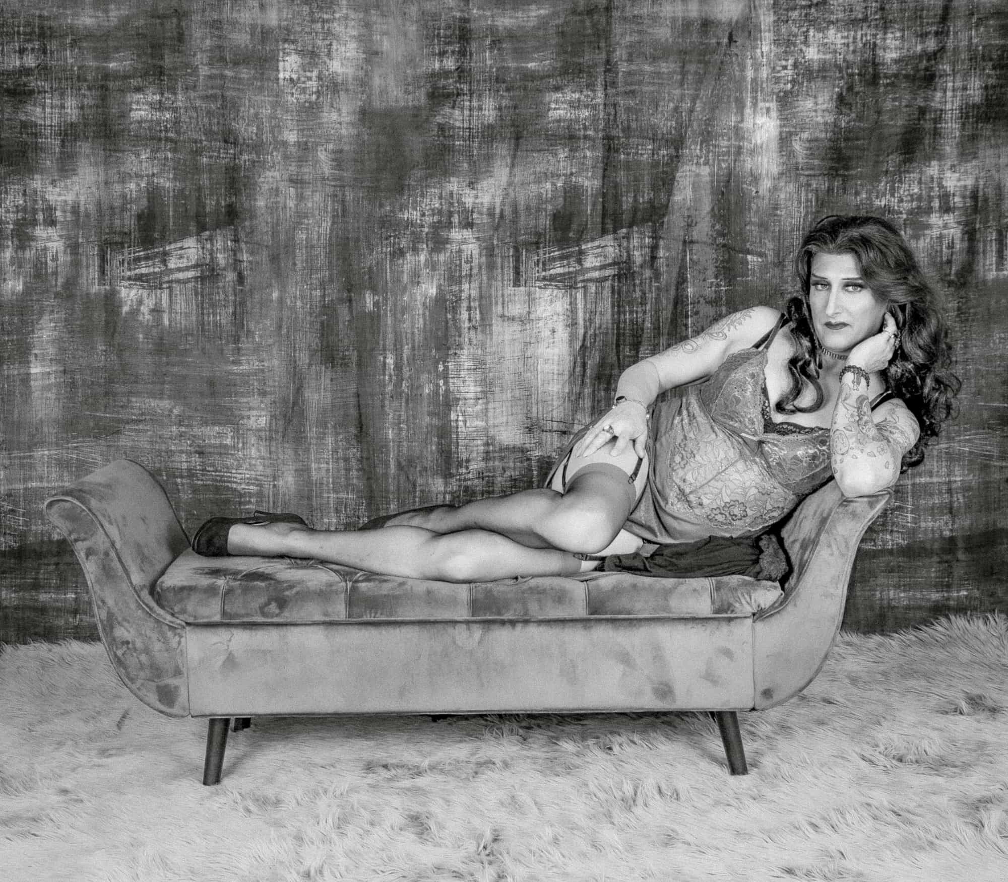 Sensual confidence radiates from woman reclining in lingerie on plush velvet chaise lounge.