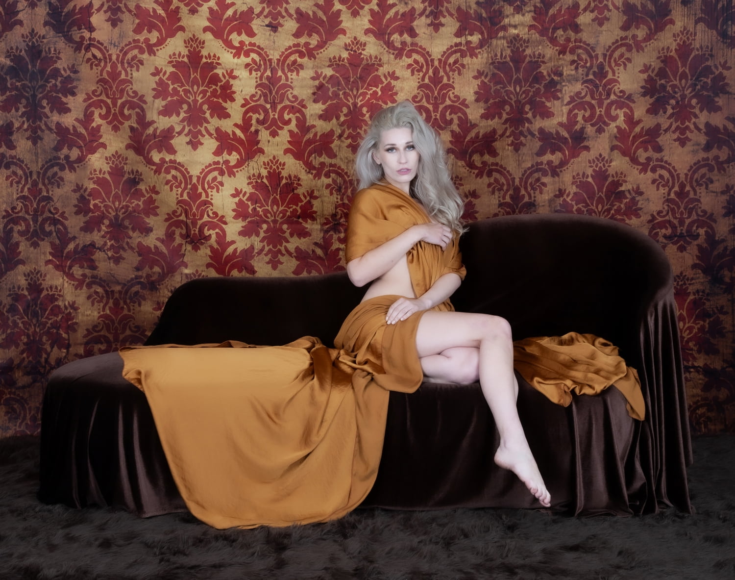 Sophisticated woman in elegant orange dress embodies luxury and intimacy on velvet couch.