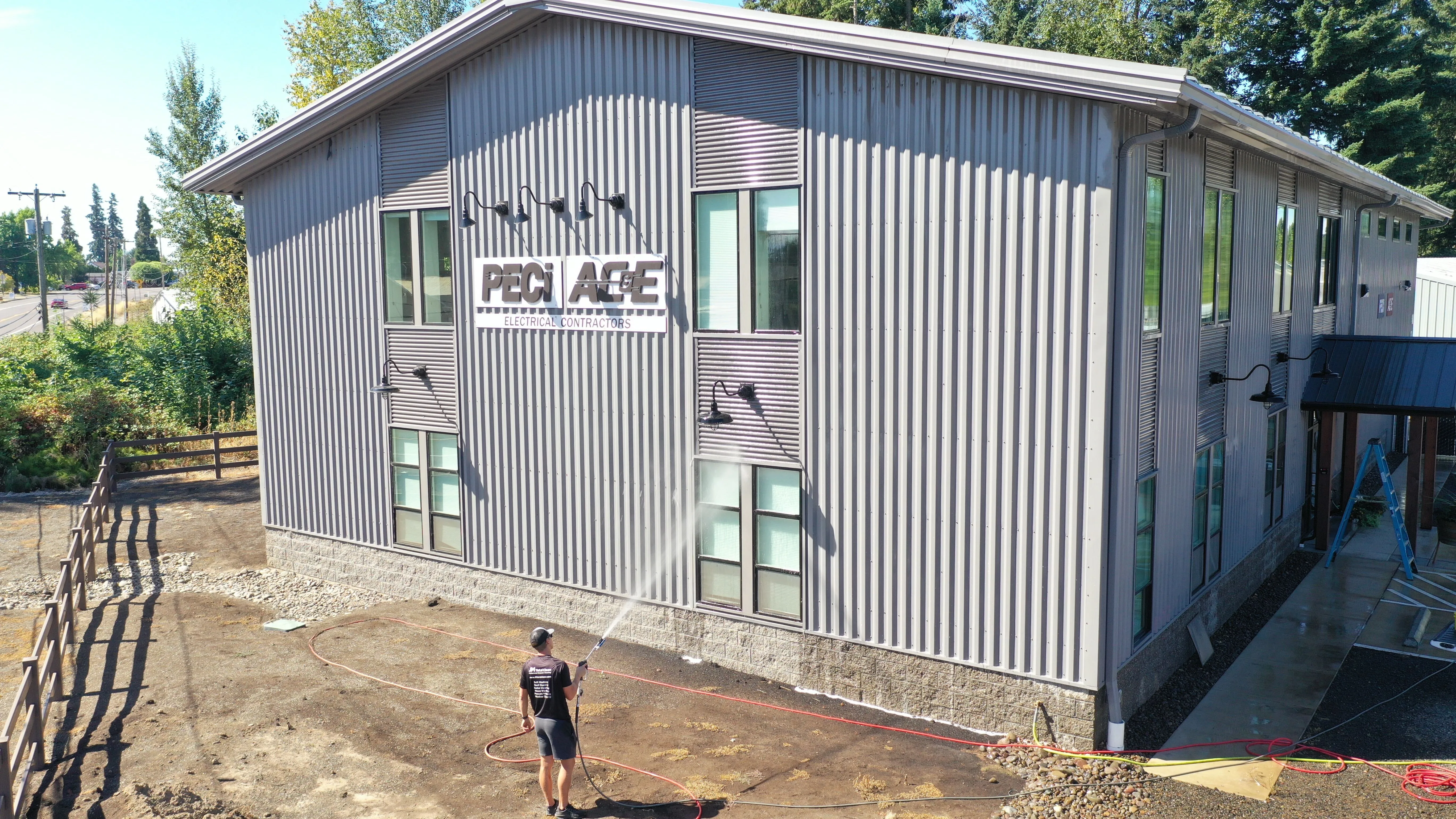 Person using a hose to spray water on a large gray metal building.