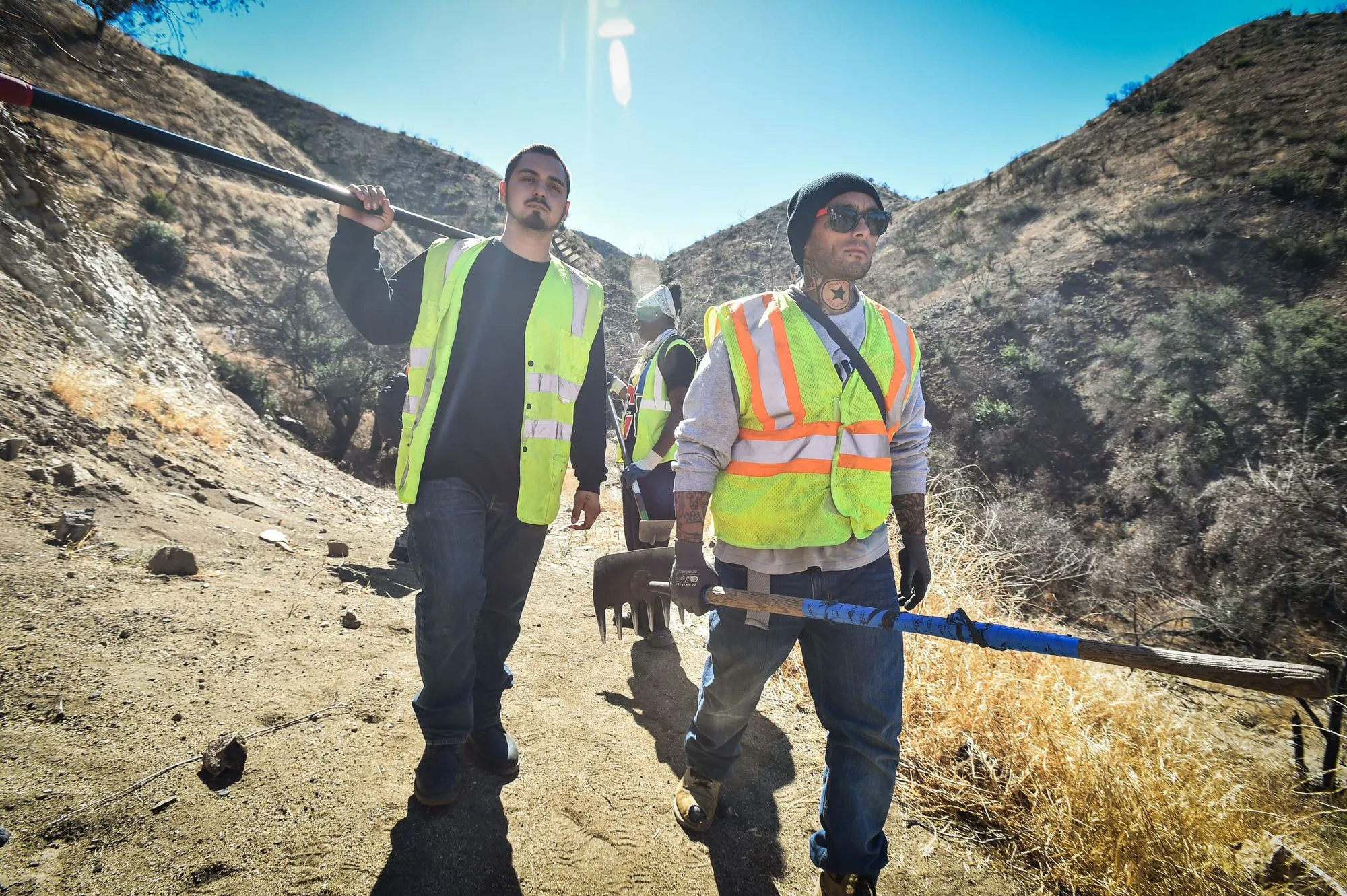 Two men in hazard vests walking down mountain side.