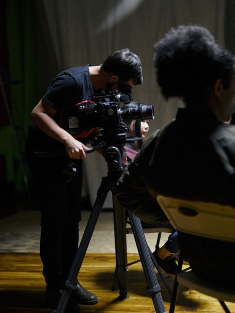 A camera operator adjusts a cinema camera on a tripod on a small set