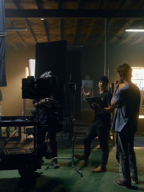 A small crew gathers around a laptop between takes on set