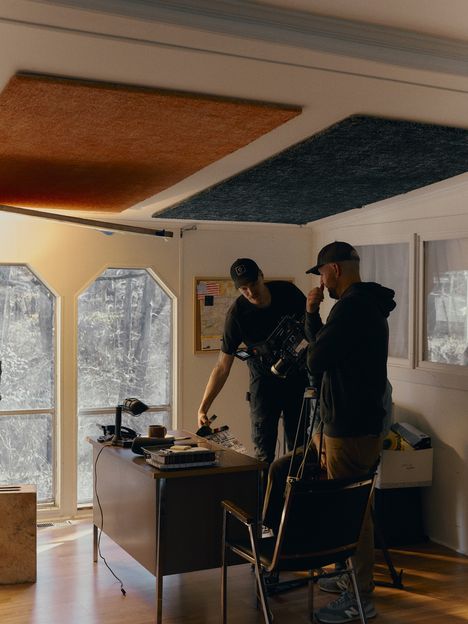 Two crew members set up a camera in a window-lit room during a prep day
