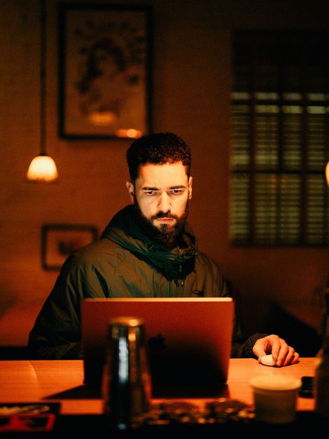 A filmmaker works at a laptop by lamplight in a warm room