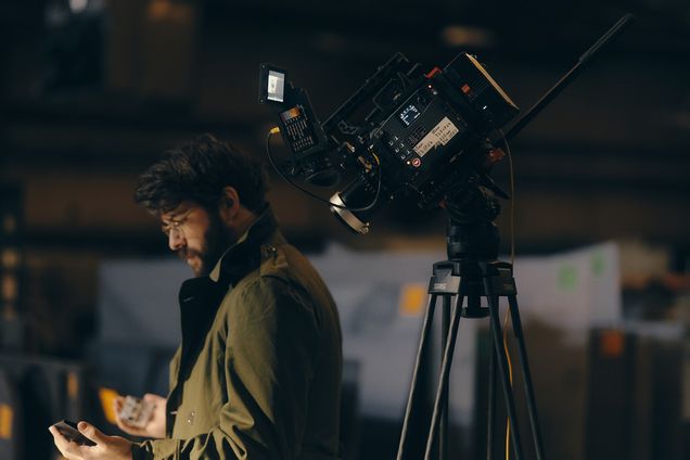 A filmmaker checks a phone next to a cinema camera on a tripod