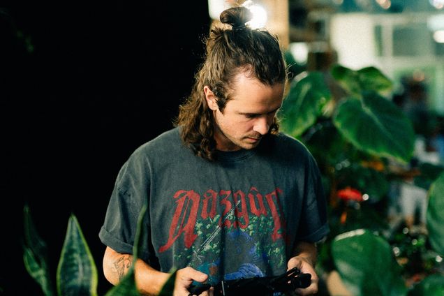 A filmmaker operates a gimbal controller surrounded by plants