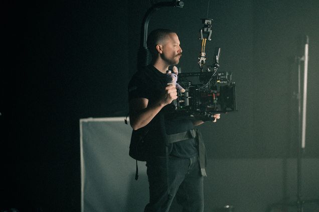 An operator holds a camera rig against a white cyclorama wall