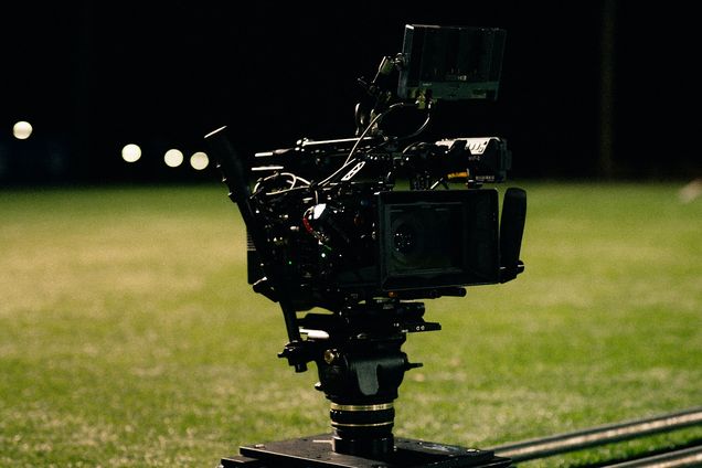 A cinema camera sits on a dolly track at the edge of a lit field