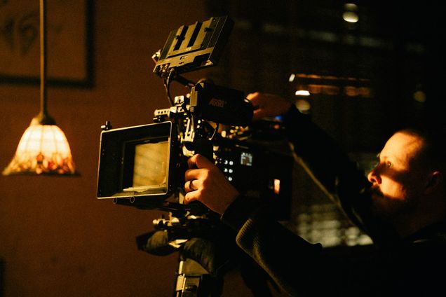 A camera operator works in a warm lamplit interior