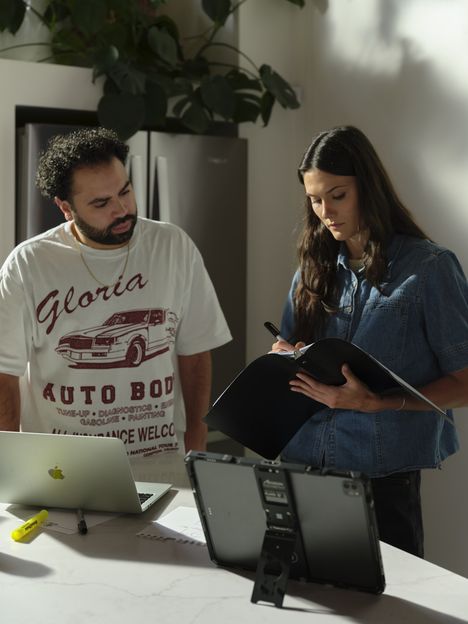 Two filmmakers reviewing notes on a clipboard beside a tablet on a stand