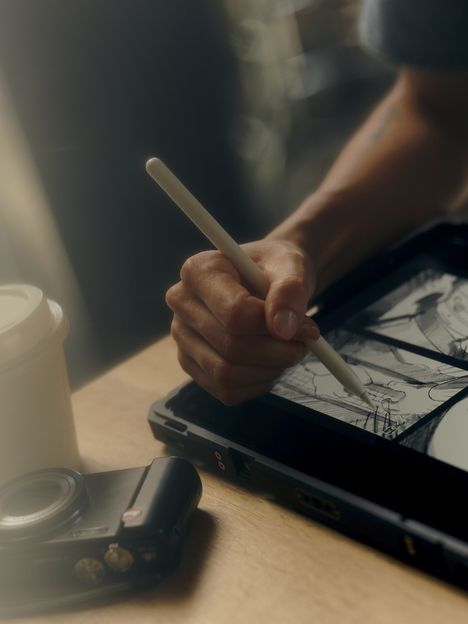 A hand drawing storyboard panels on a tablet with a stylus