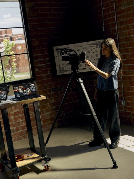 A filmmaker adjusting a cinema camera on a tripod in a brick studio