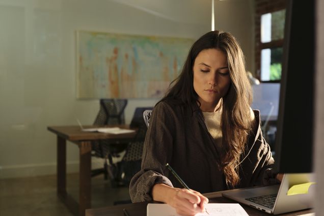 A filmmaker writing at a desk in a daylit studio