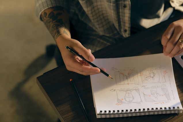 A hand sketching storyboard panels in a spiral notebook