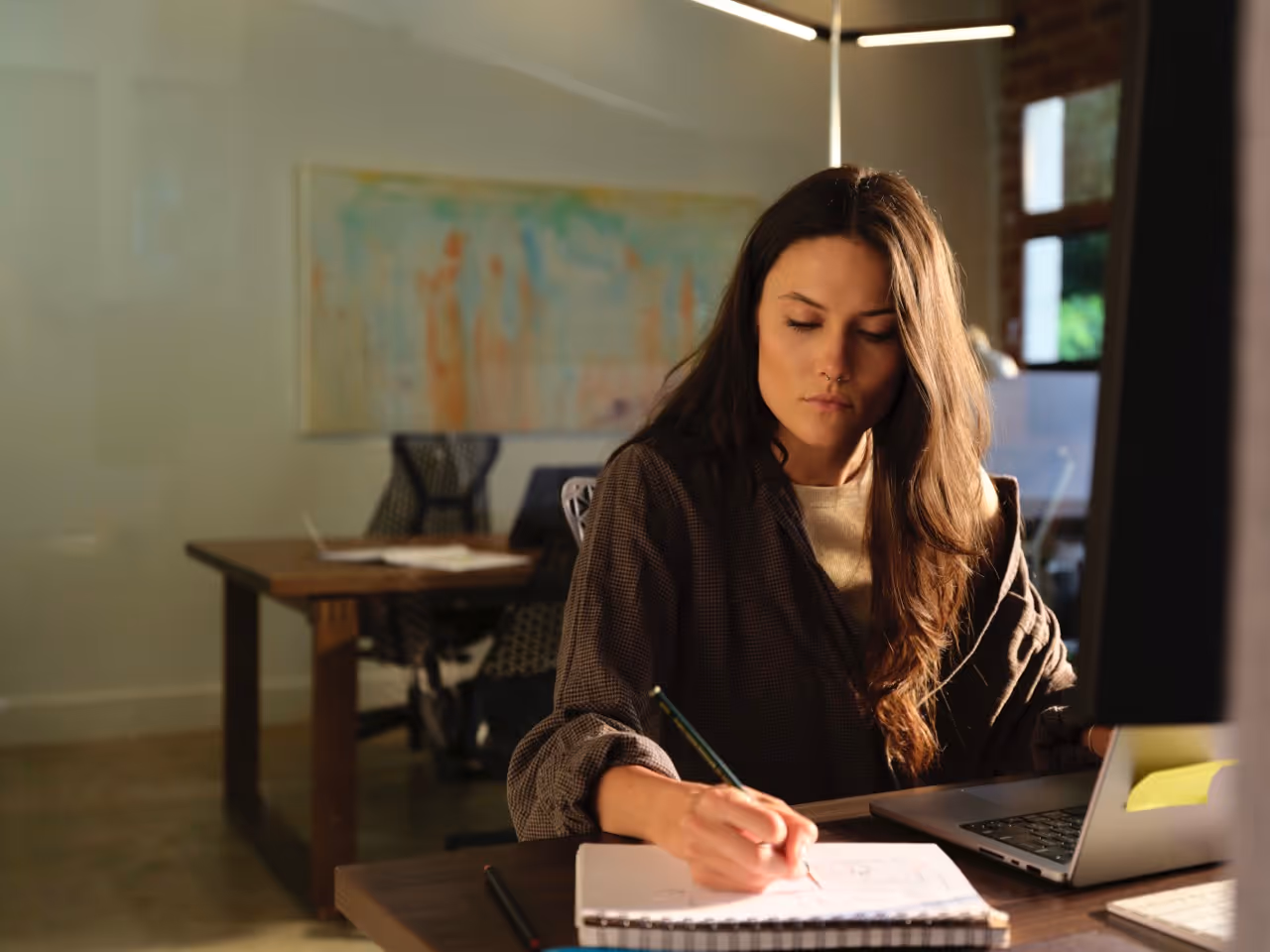 A woman sitting at a desk writing on a notepad.