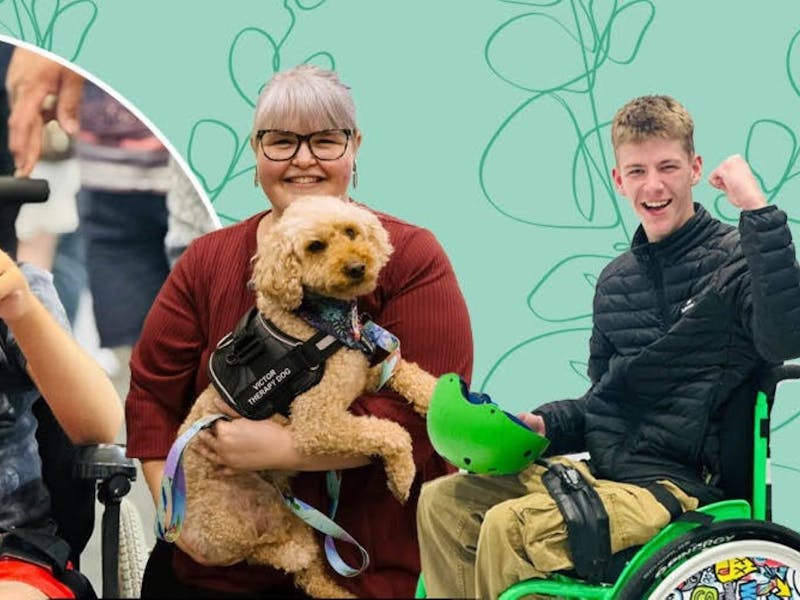 A lady holding a gold coloured service dog and a man in a wheelchair with his fist in the air