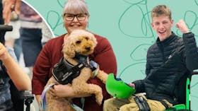 A lady holding a gold coloured service dog and a man in a wheelchair with his fist in the air