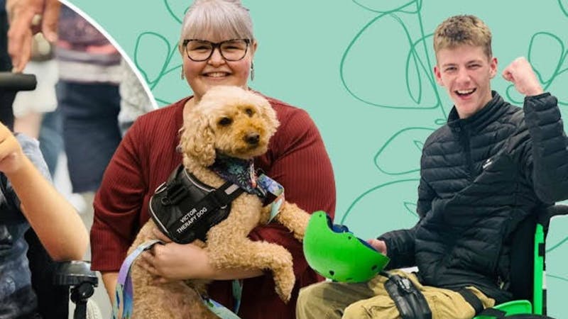 A lady holding a gold coloured service dog and a man in a wheelchair with his fist in the air
