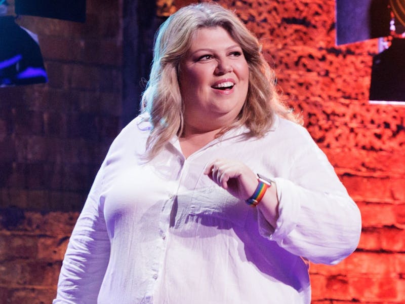 photo of Urzila in a white button up shirt smiling looking to the right, in front a brick background