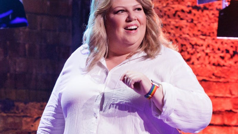photo of Urzila in a white button up shirt smiling looking to the right, in front a brick background