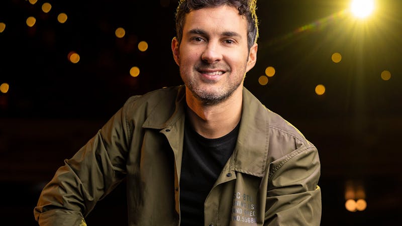 photo of mark smiling behind a black background with shining lights coming through
