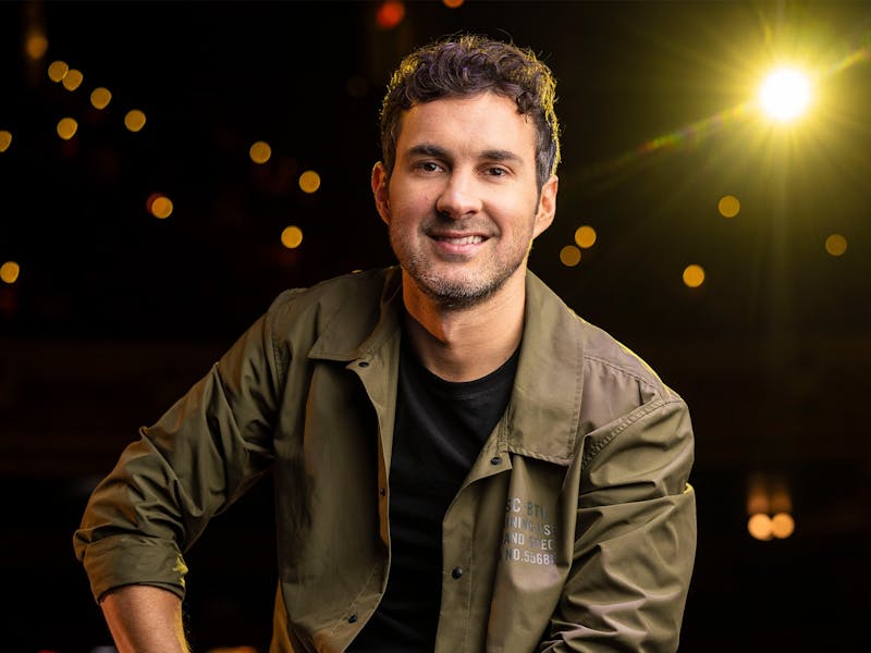 photo of mark smiling behind a black background with shining lights coming through