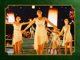 Photo of girls in white dresses dancing on a stage in front of large warm white lanterns