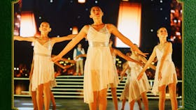 Photo of girls in white dresses dancing on a stage in front of large warm white lanterns
