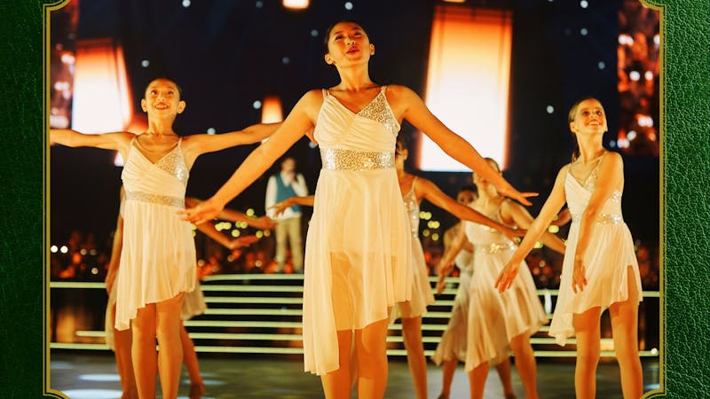 Photo of girls in white dresses dancing on a stage in front of large warm white lanterns
