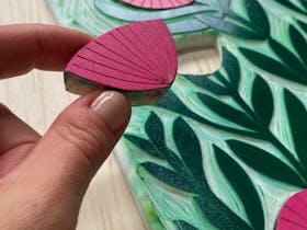 Photo of a persons hand with a craft item that is a red flower top, background shows green stems